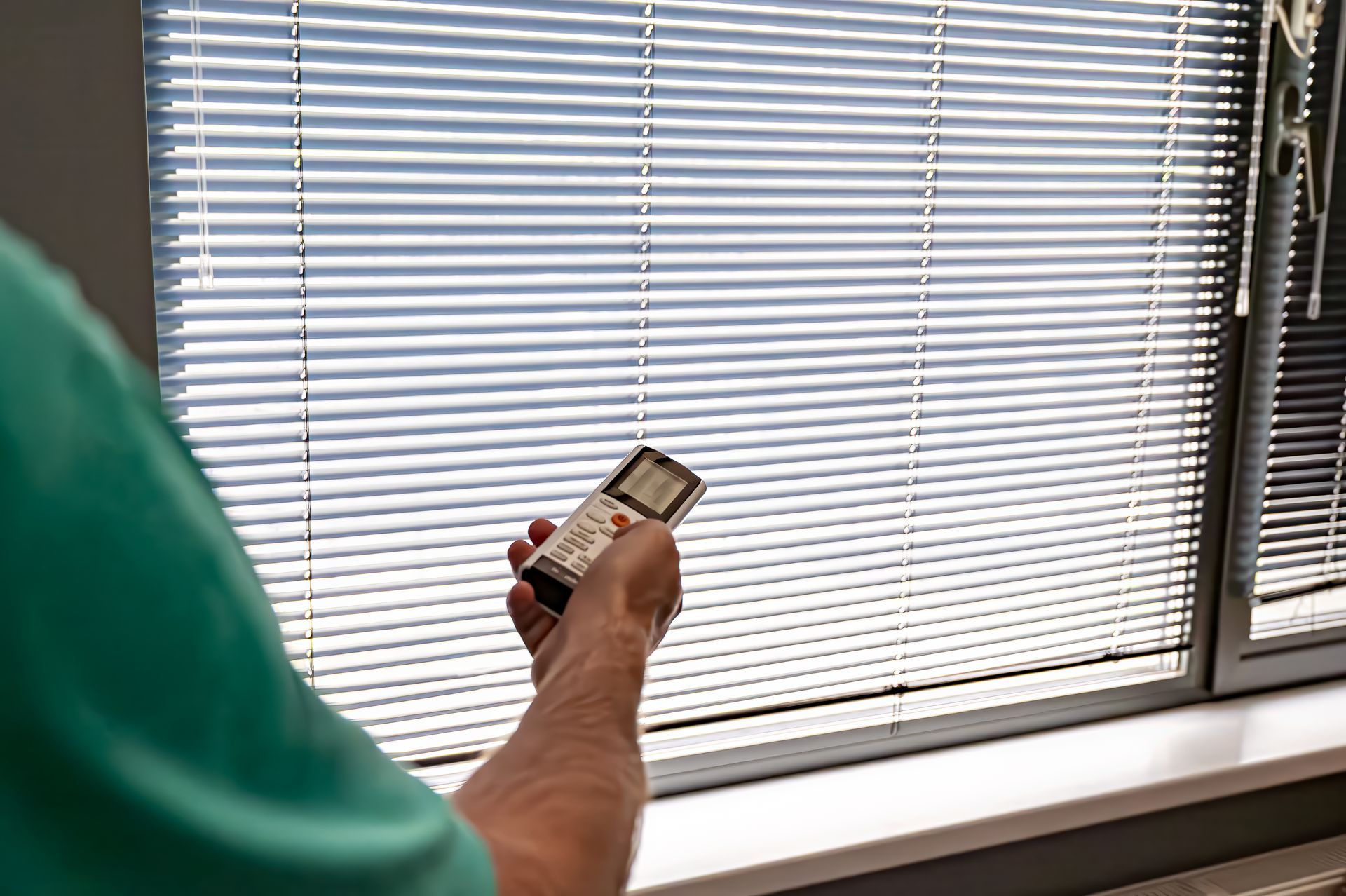 A man is using a remote control to operate blinds.