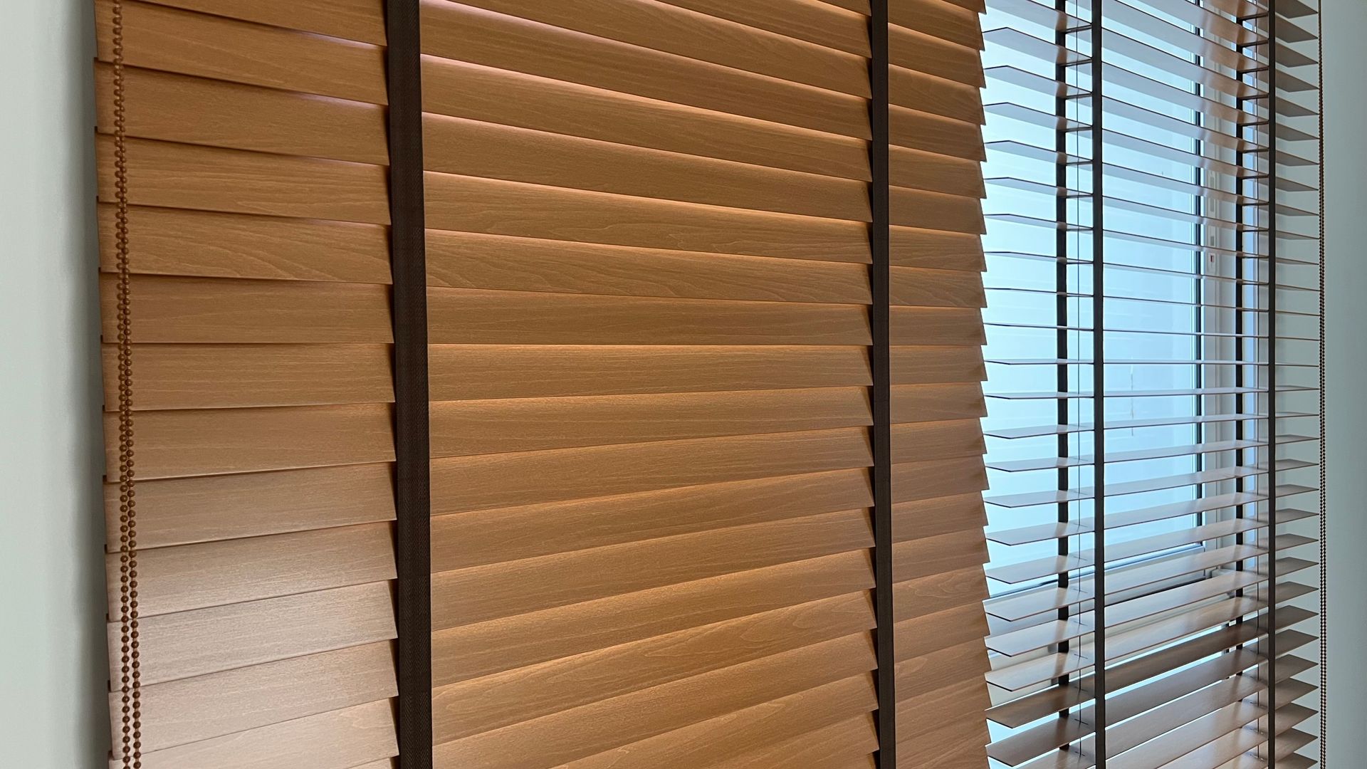 Beige window blinds partially open, with light filtering through on the right side.