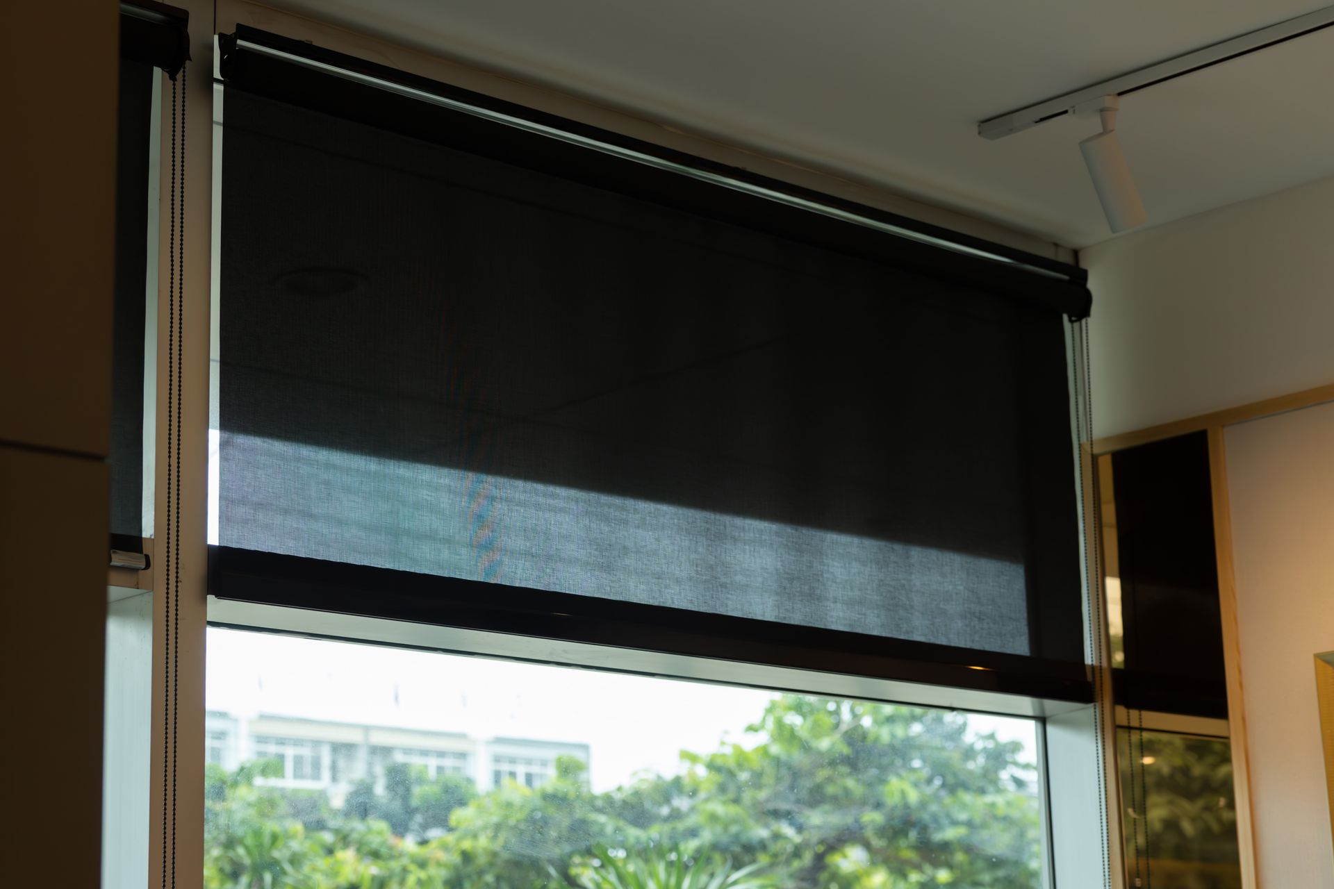A black window shade is drawn to the middle of a window at a residence