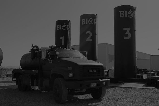 Una fotografía en blanco y negro de un camión estacionado frente a tres tanques.