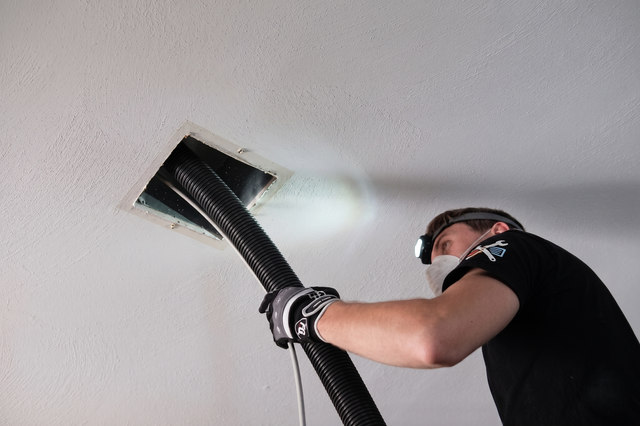 Worker installing black ducting in a ceiling vent opening