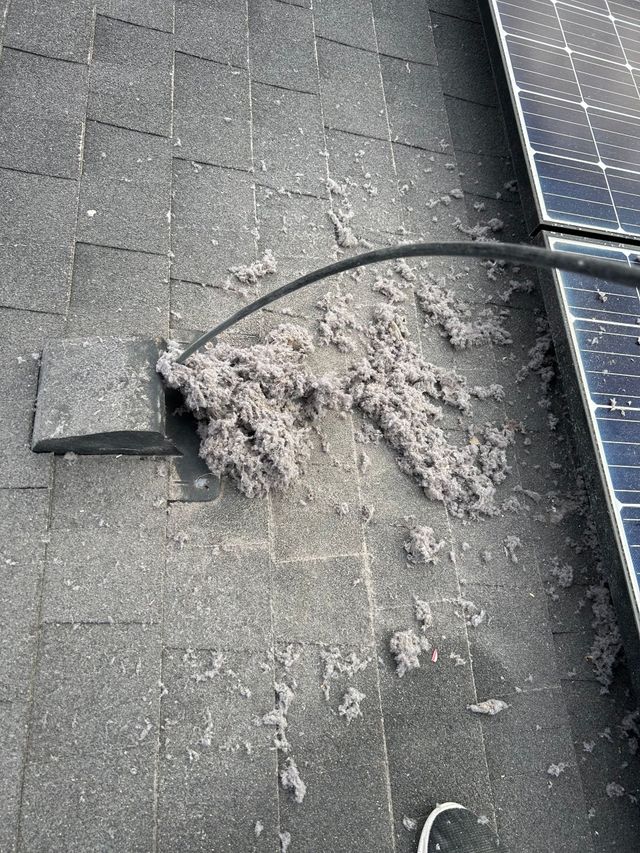 Damaged asphalt roof with a pile of debris near a black cable and solar panel edge
