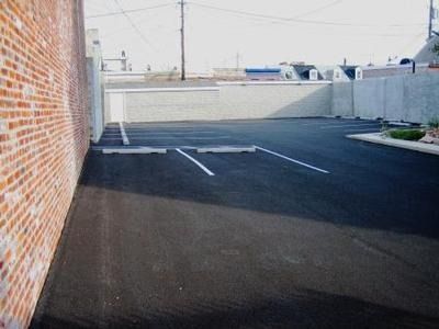 Empty asphalt parking lot next to a brick wall and a gray concrete wall.