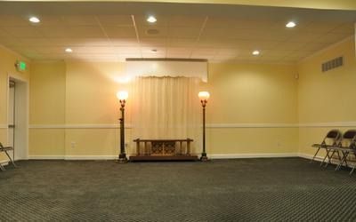 Empty funeral home chapel with dark carpet, light walls, and draped backdrop.