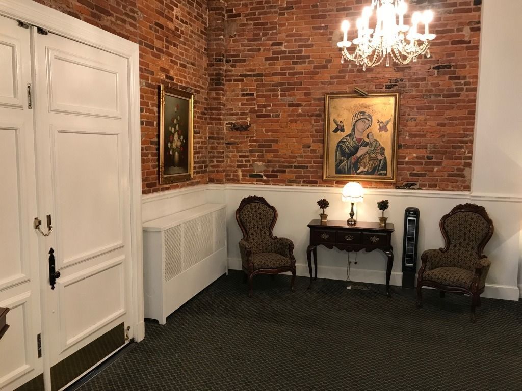 Interior room with exposed brick wall, ornate chandelier, two patterned chairs, and framed art.