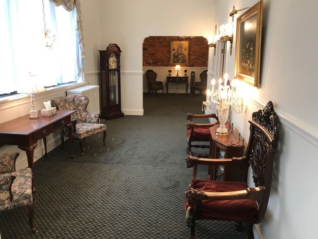 Hallway with antique furniture, carpet, artwork, and lighting; likely a funeral home.