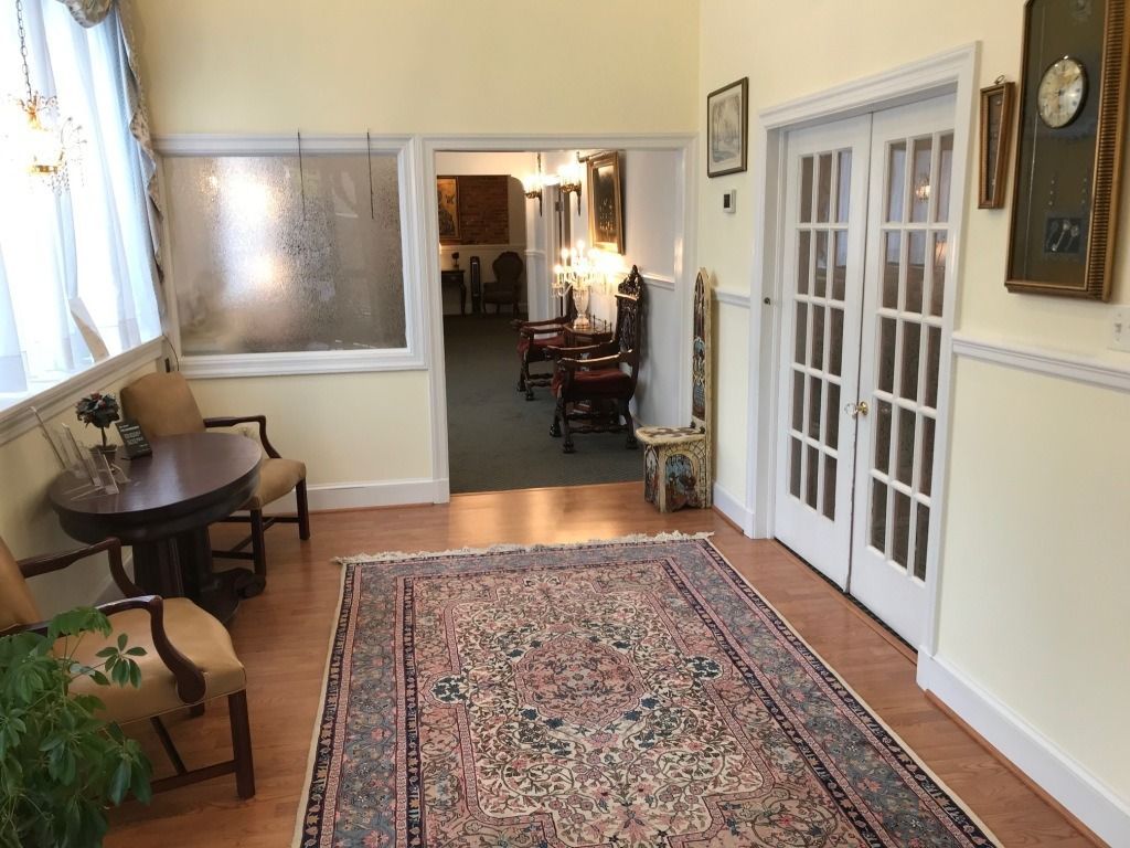 Hallway with rug, chairs, table, and doors leading to another room.