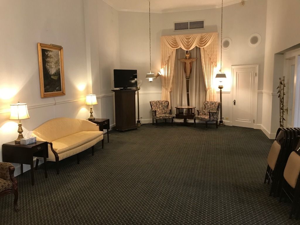 Funeral home interior, room with chairs, sofa, cross on wall, and soft lighting.