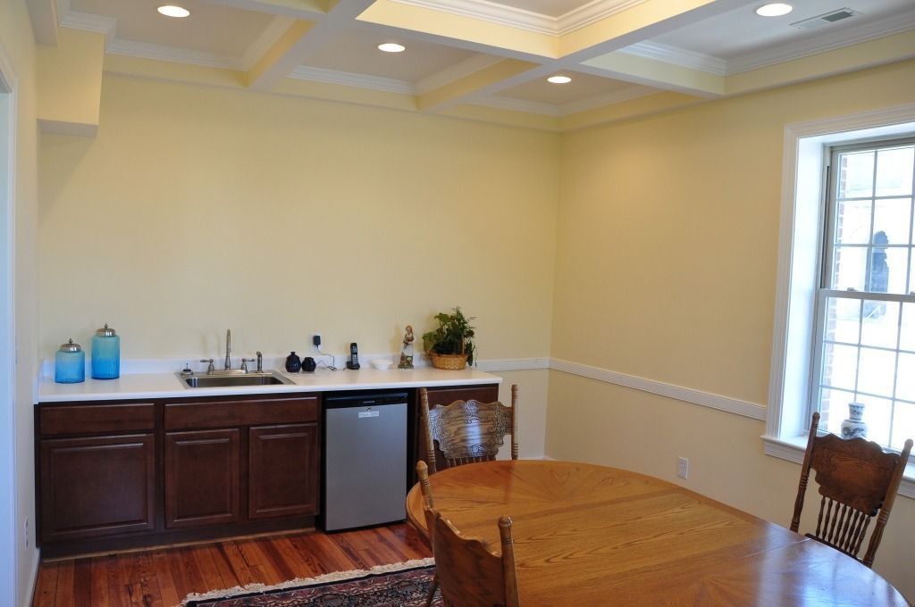 A small dining room with a wet bar, oval table, and two wooden chairs. Light yellow walls and a coffered ceiling.