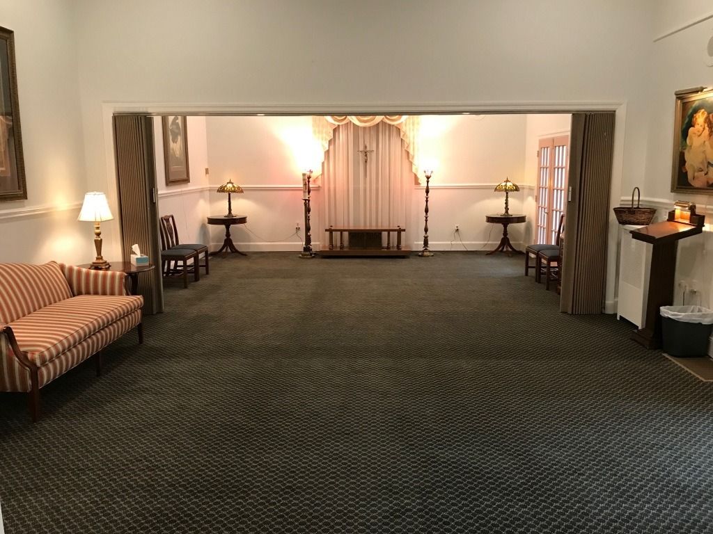 Funeral home interior, with a sofa, chairs, and a central altar.  Dark carpet and neutral walls.