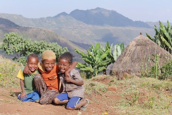 A group of children are posing for a picture in a field with mountains in the background.