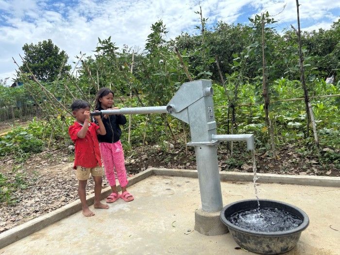 A boy and a girl are standing next to a water pump.
