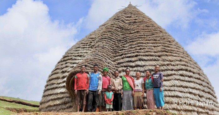 A group of people are posing for a picture in front of a thatched building.