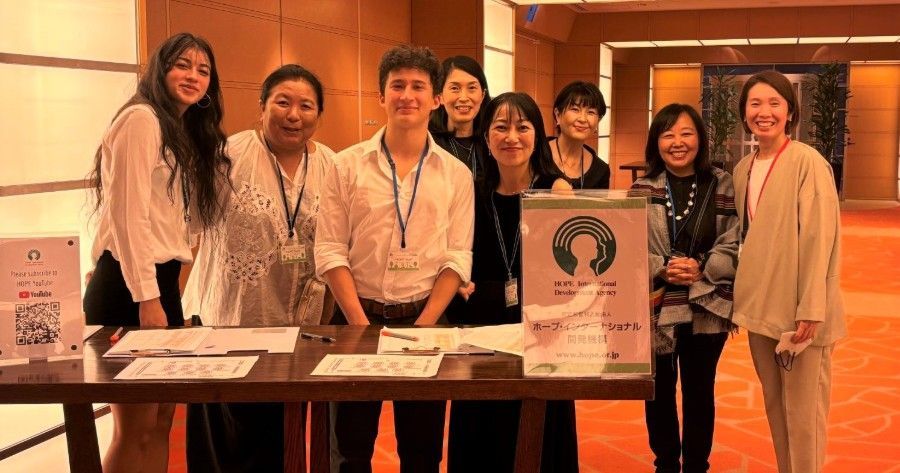 Group of people smiling at a registration table. Attendees are diverse, in a well-lit hall.
