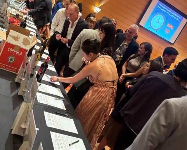 People bidding at an event, leaning over tables with auction items and bid sheets.