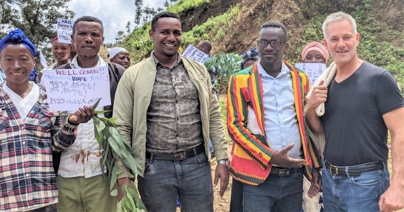 Group of people holding signs outdoors, smiling, some with foliage.