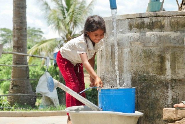 Child washing clothes at an outdoor concrete basin with a blue bucket and water