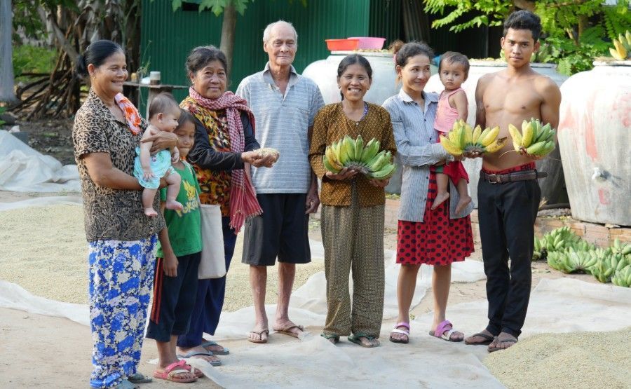 Group of people standing outdoors, holding baskets of colorful produce and greens on a path near a building