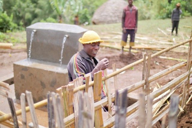 Worker in a yellow hard hat stands beside wooden scaffolding at a construction site.