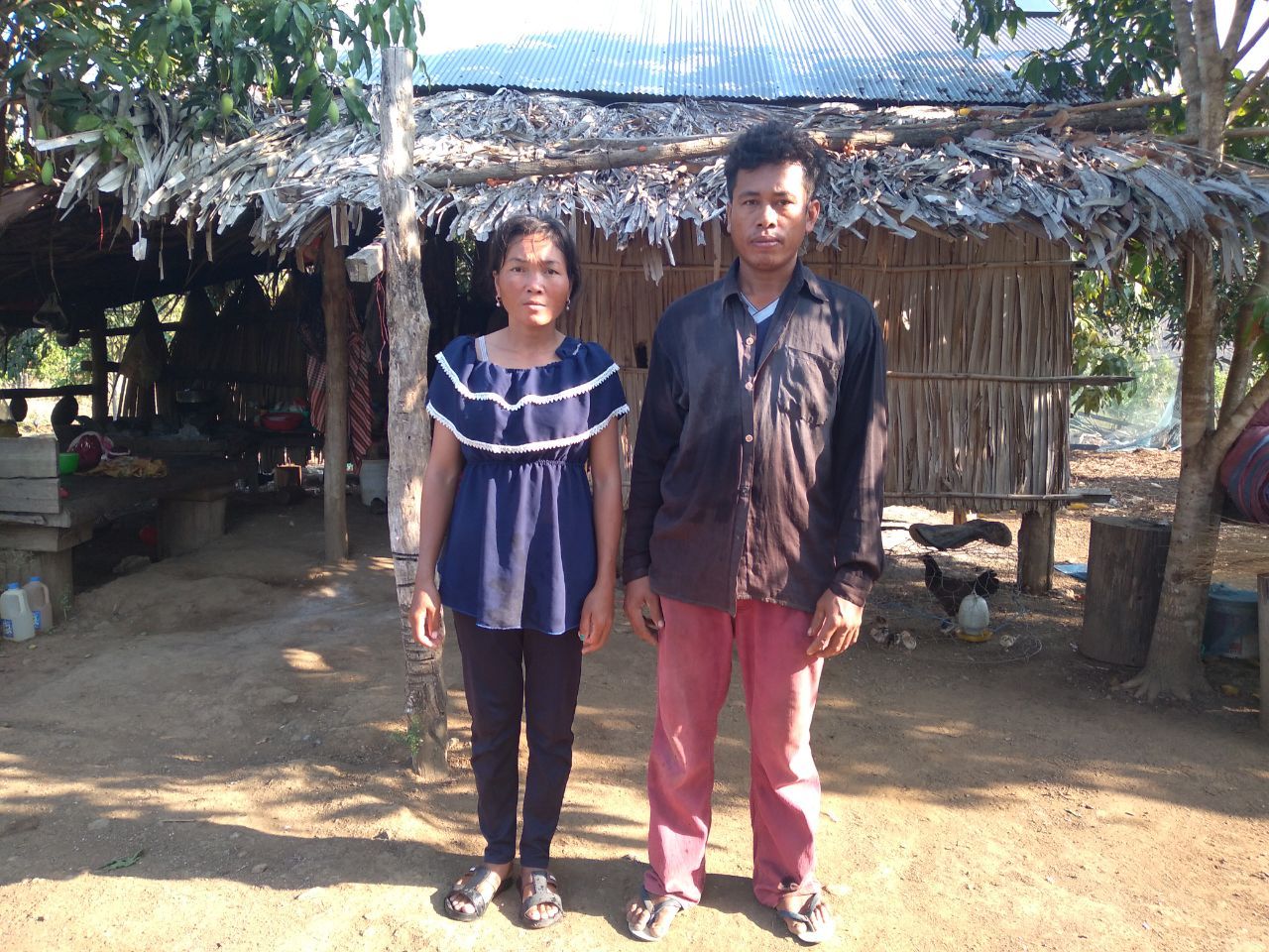 A man and a woman are standing in front of a hut.