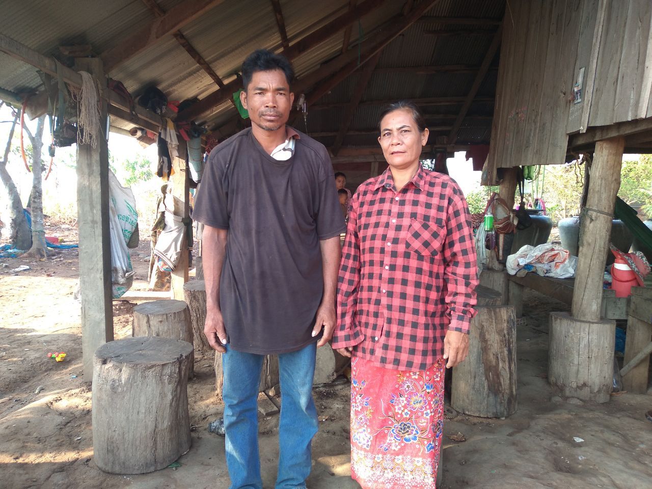 A man and a woman are standing next to each other in front of a hut.