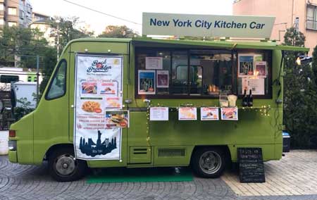 A green food truck is parked on the side of the road.