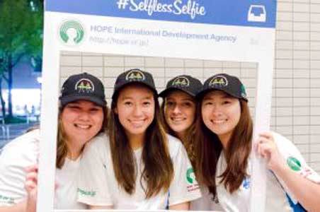 A group of young women are posing for a picture with a selfie frame.