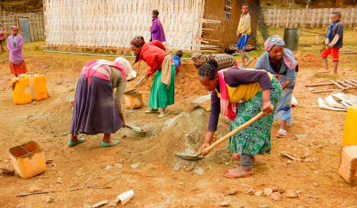 Women of the village of Kuta help with the mixing of sand and cement