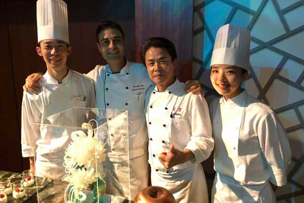A group of chefs are posing for a picture in front of a cake.
