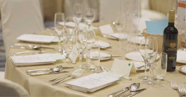 A table is set with plates , utensils , glasses and a bottle of wine.