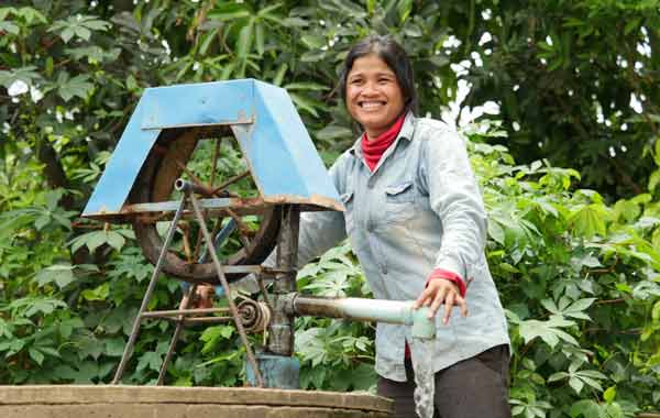 A woman is smiling while pumping water from a well.