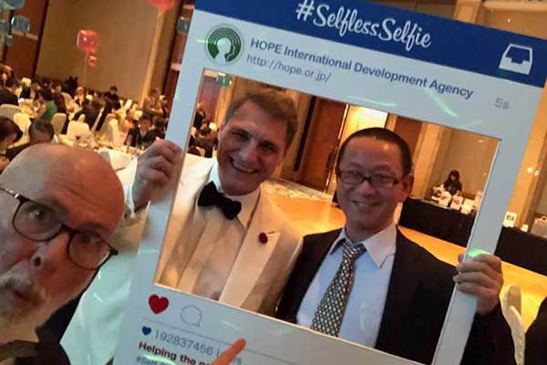 Two men are posing for a picture with a frame that says selfless selfie