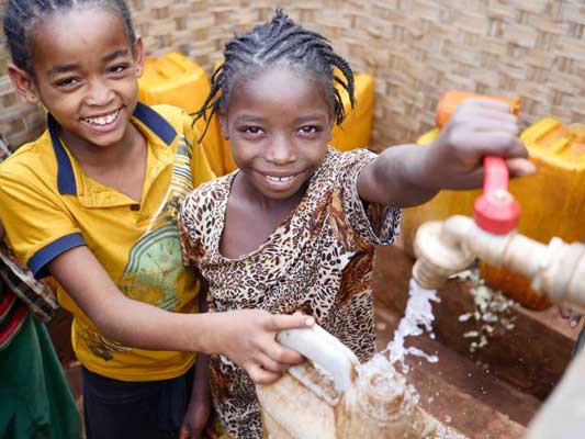 A boy and a girl are washing their hands in a faucet.
