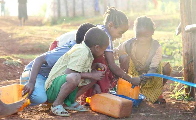 A group of children are playing with water bottles on the ground.