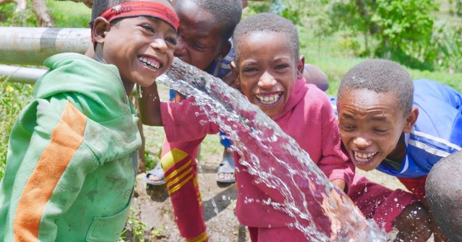 Children laugh as water sprays, outdoors.
