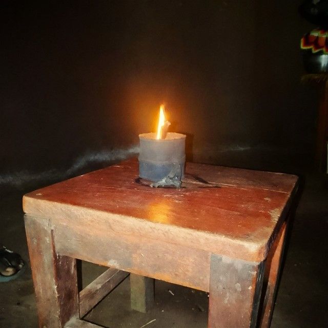Small lit candle in a metal cup on a wooden table in a dark room