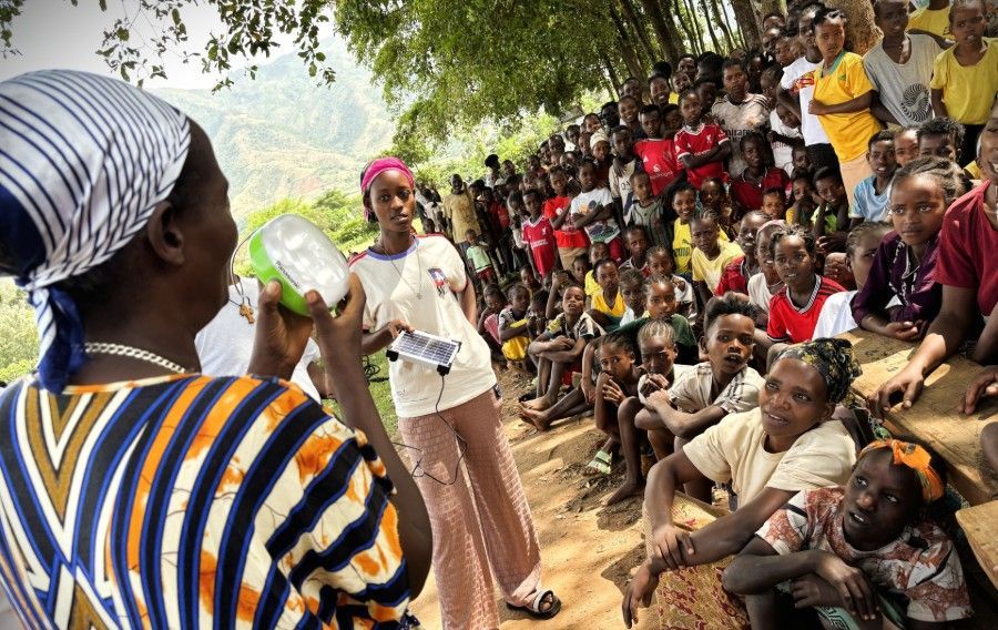 Woman speaking with a megaphone to a seated outdoor crowd under trees