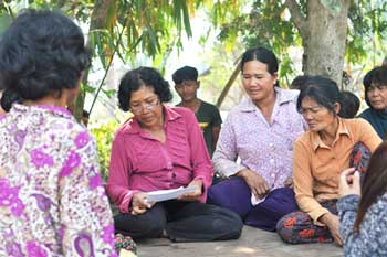 A group of women are sitting on the ground under a tree.