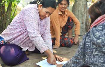 A group of women are sitting on the ground looking at a piece of paper.