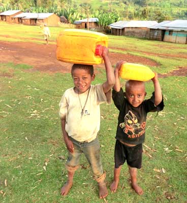 Two young boys are carrying large yellow containers on their heads.