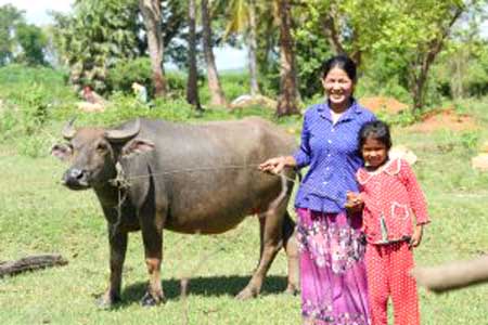 A woman and a child are standing next to a water buffalo in a field.