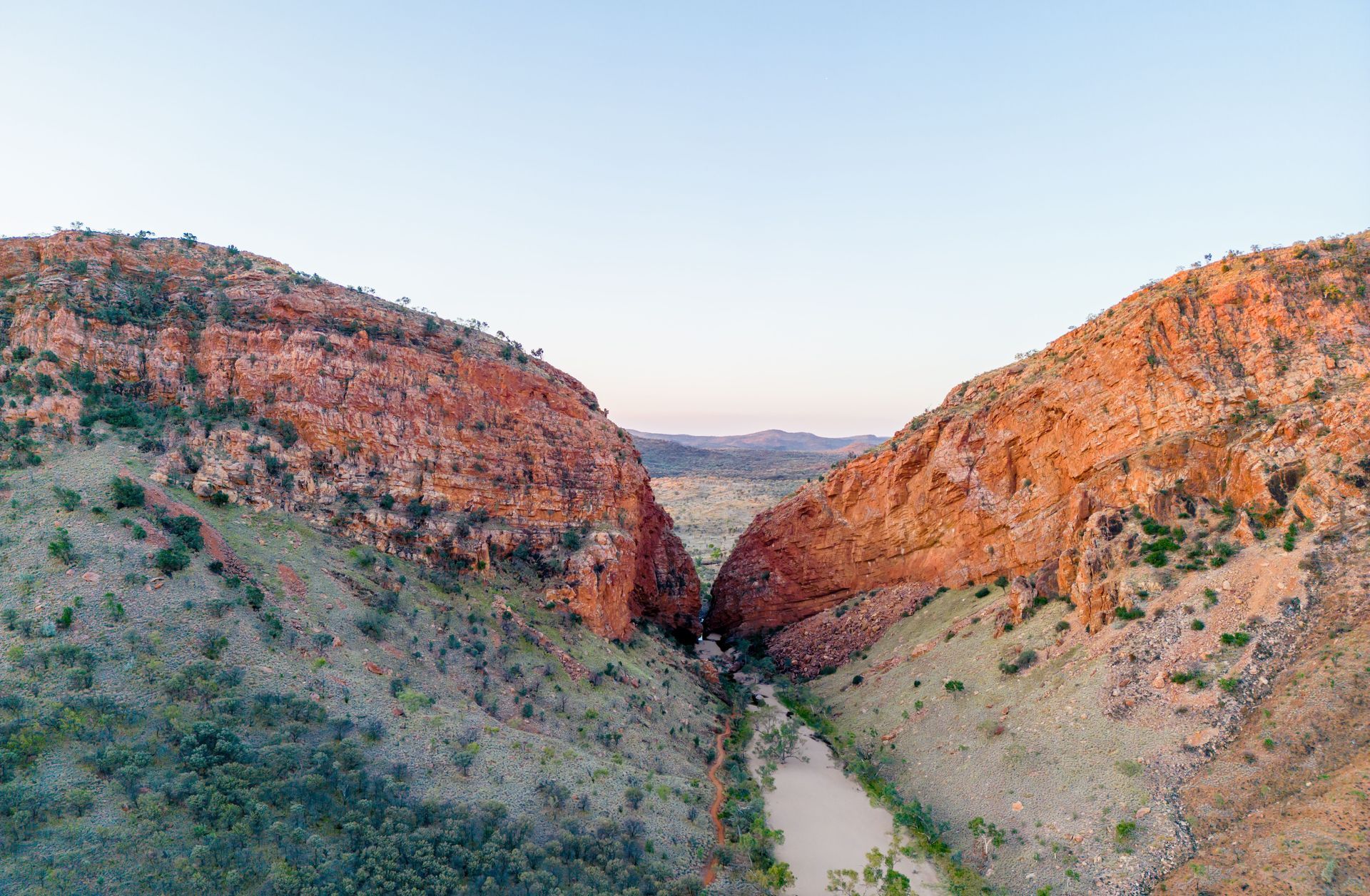 Red rock canyon, a river flows through, under a light blue sky.