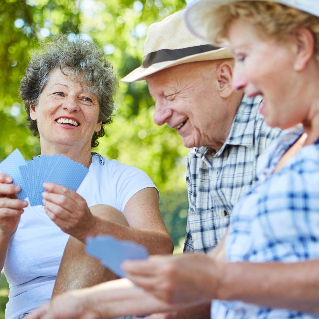 Three people playing cards and smiling outdoors.
