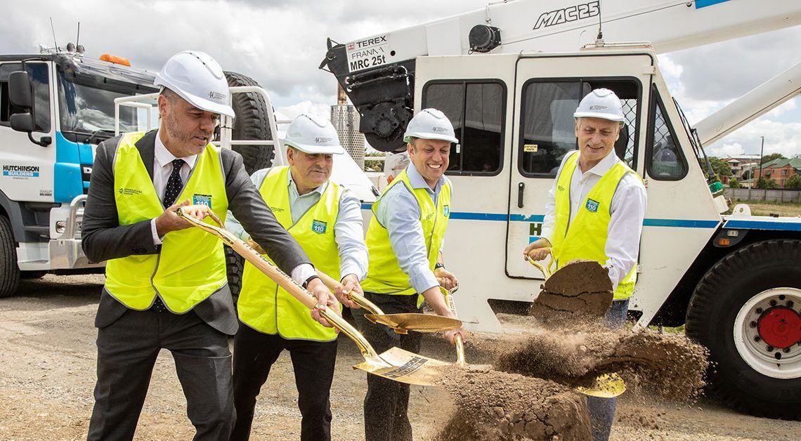 Four men in business wear, hard hats and high visibility vest as shovelling direct as they stand in front of two trucks