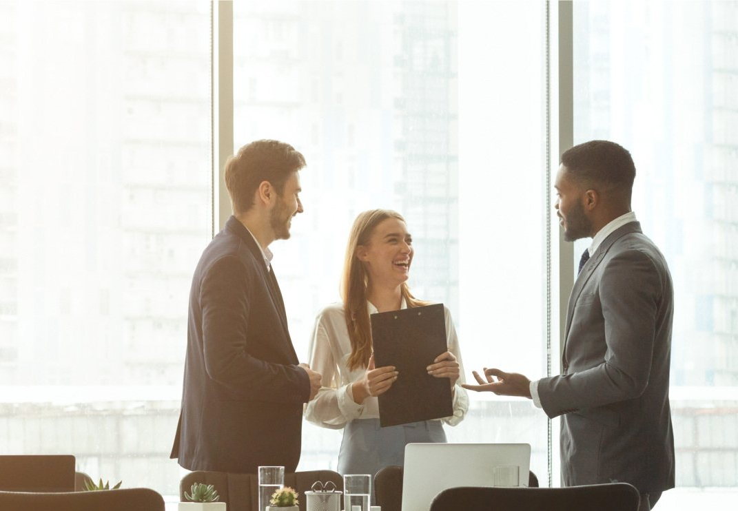 Two men and one women laughing and having a business meeting by a window