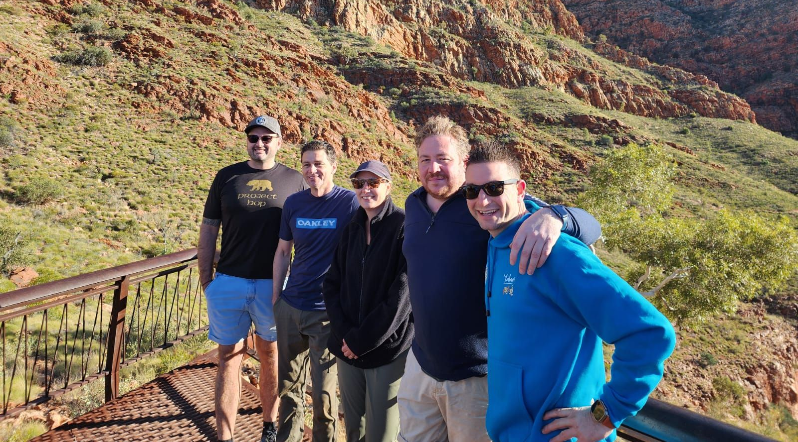 Group of people smiling in front of Uluru, Australia at sunset; red rock, brown landscape, sunny day.