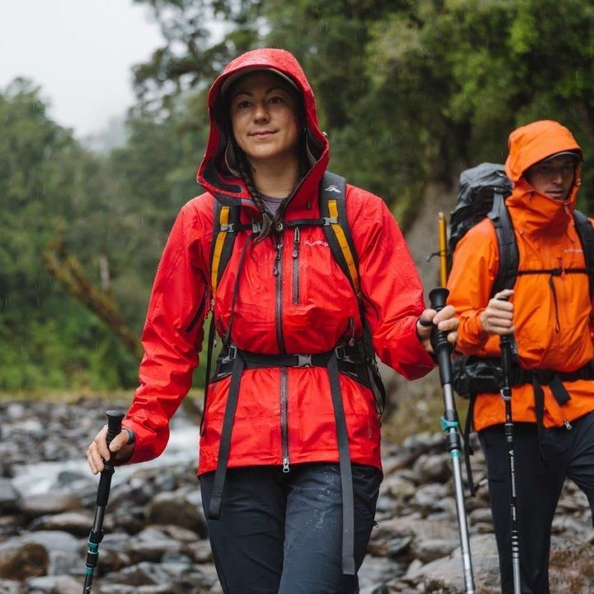 A man and woman hiking in an area that was recently raining, with river stones, trees and fog in the background.