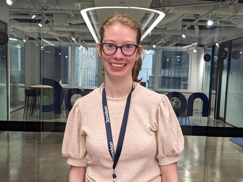 Lily from Davidson Melbourne office standing in front of glass doors with Davidson logo on them.