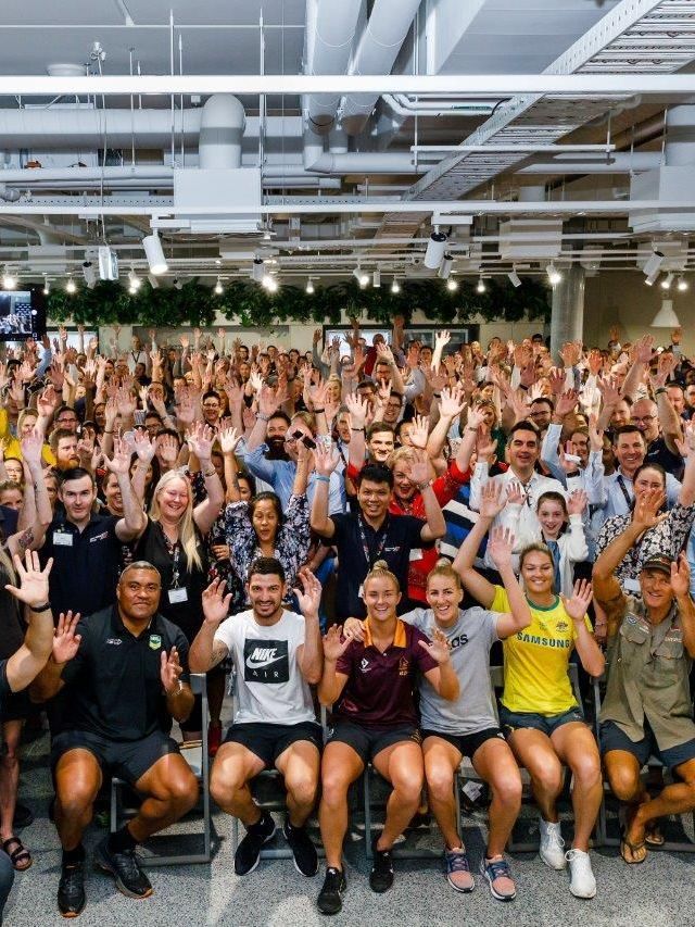 A large crowd of people in a hug room raising their hands above their heads.