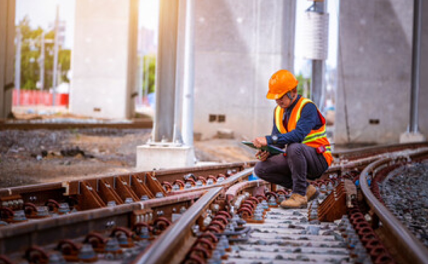 Man crouching by railway line with clipboard and hard hat